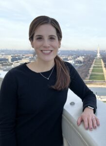 Photo from the waist up of Katrina Notarmaso, an educator and legislative fellow dressed in a black dress with long sleeves, who is part of ExcelinEd's first Education Policy Resident program. The Washington Monument and National Mall are in the background. 
