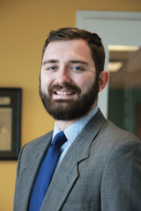 Photo from the torso up of Ryan Dellinger, a public policy advocate dressed in a gray suit with a light blue dress shirt and dark blue tie, who is part of ExcelinEd's first Education Policy Resident program.